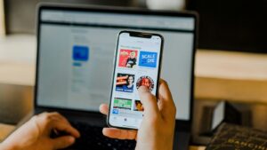 A person using a smartphone to browse podcast options about marketing strategies while working on a laptop in the background.