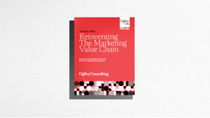 A red and white book titled "Reinventing The Marketing Value Chain" by Ogilvy Consulting lies on a light gray surface.