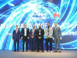 Seven men in business attire stand in front of a large digital display featuring the Omantel and Huawei logos at a technology summit.