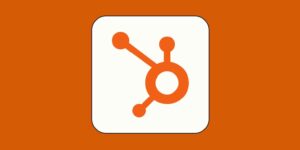 An orange HubSpot logo with three connected nodes appears on a white square background set against an orange backdrop, symbolizing the brand’s AI capabilities.