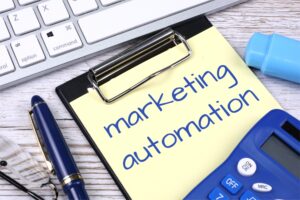 A clipboard with a note reading "marketing automation" sits next to a keyboard, highlighter, calculator, pen, and glasses—ideal tools for B2B brands embracing set it and forget it strategies.