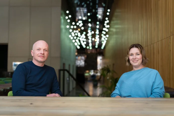 Havas sit at a wooden table in a modern indoor space with hanging lights and wood-paneled walls.