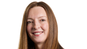 A woman with straight, long brown hair smiles at the camera against a plain white background, embodying the confidence of a senior hire driving sustained growth at Acquirz.
