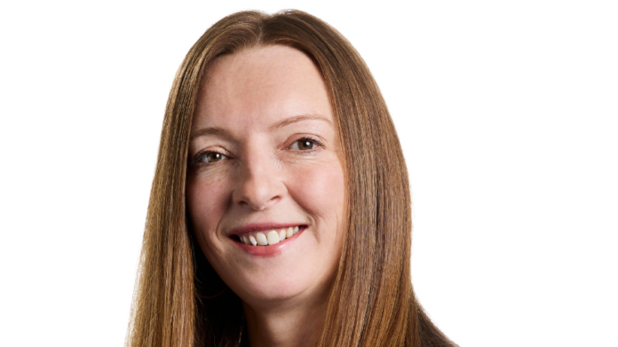 A woman with straight, long brown hair smiles at the camera against a plain white background, embodying the confidence of a senior hire driving sustained growth at Acquirz.