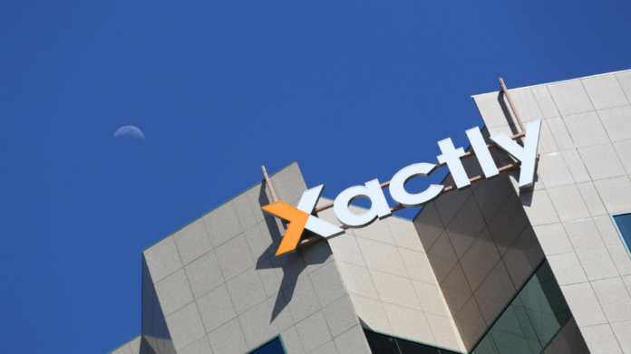 A modern building with the Xactly logo on its facade, set against a clear blue sky where the moon rises—reflecting Xactly’s innovation in AI-powered SPM solutions.