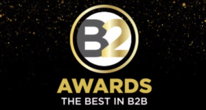 A circular B2 Awards logo with gold, black, and white colors, and the text "AWARDS THE BEST IN B2B" below on a black background with gold specks.