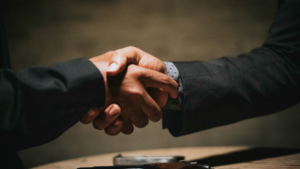 ABM: Two people in business attire shake hands over a table, suggesting an agreement or partnership at a key stage of the buyer journey.