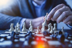 lead generation tactics. A person in a suit moves a white king piece on a chessboard, symbolizing strategic 2025 lead gen tactics, with other chess pieces arranged on the board and some toppled over.