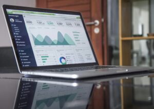 A laptop displays an analytics dashboard with charts, graphs, and data metrics on the screen—ideal for marketers tracking performance or avoiding lead qualification mistakes—situated on a reflective desk in an office setting.