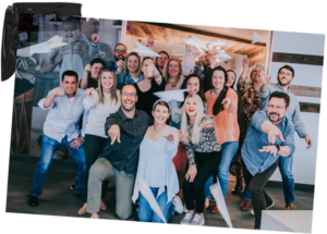 A group of people indoors, including members from B2B agencies like Littlefield, smile and throw paper airplanes toward the camera, posing together in a casual setting.
